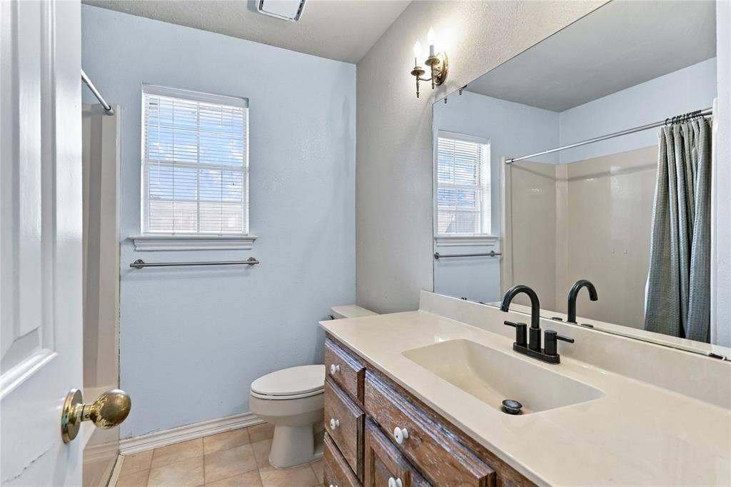 1309 Oxford Lane, Denton, TX 76209 Light-toned wall paint with a window, vanity with a light-colored countertop, built-in sink, and a black-finish faucet