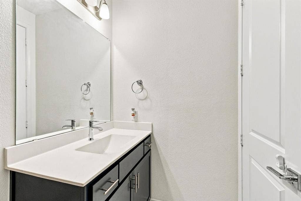 2812 Dunbar Drive, Northlake, TX 76247 Vanity featuring an integrated rectangular sink with chrome faucet, a white countertop, and dark wood-finish cabinetry with chrome hardware