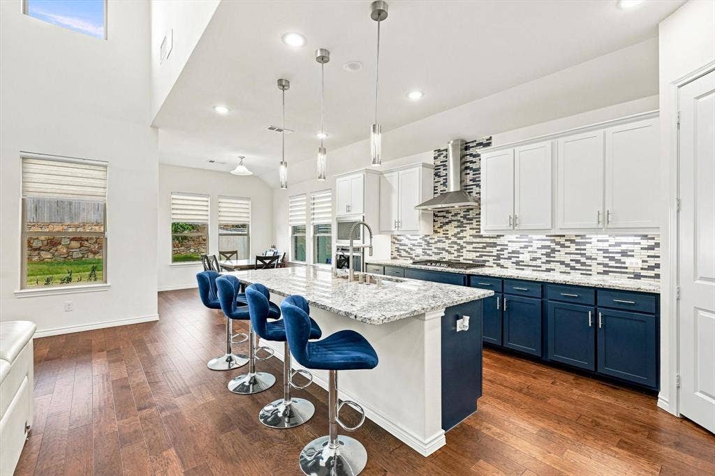 2812 Dunbar Drive, Northlake, TX 76247 Open-concept kitchen with a large island featuring a stone countertop, wood-finish flooring, two-tone cabinetry, and stainless steel appliances