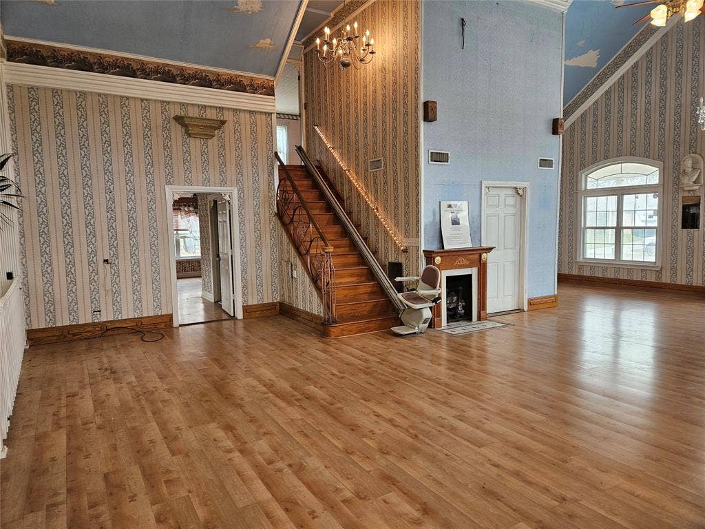716 Dogwood Street, Robinson, TX 76706 Unfurnished living room featuring wallpapered walls, a high ceiling, crown molding, wood finished floors, and a fireplace with flush hearth