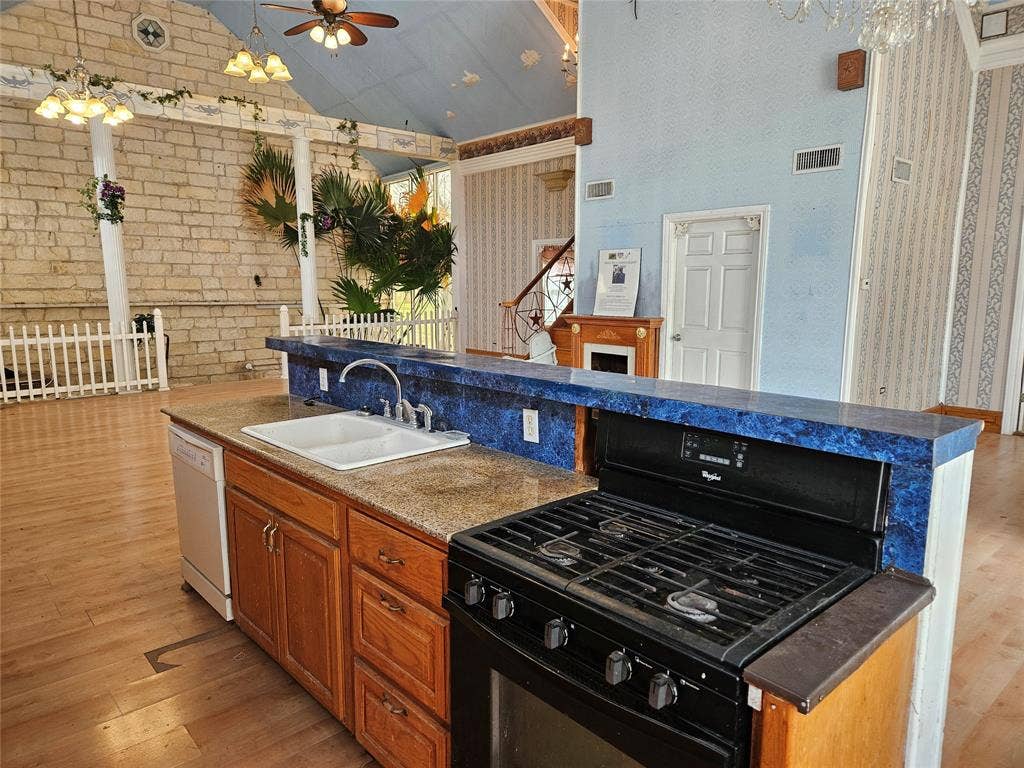 716 Dogwood Street, Robinson, TX 76706 Kitchen featuring black gas range, wood finish cabinets, light wood-style floors, brick wall, and a high ceiling