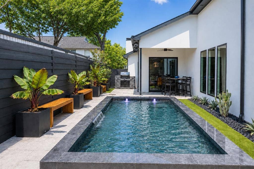 939 N Buckner Boulevard, Dallas, TX 75218 Outdoor living space featuring a rectangular pool with water features, a built-in outdoor kitchen, a covered patio, and a dark wood fence
