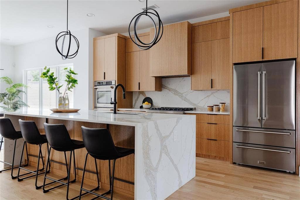 939 N Buckner Boulevard, Dallas, TX 75218 Light wood-finish cabinetry and flooring, stainless steel appliances, and a waterfall island with a patterned countertop