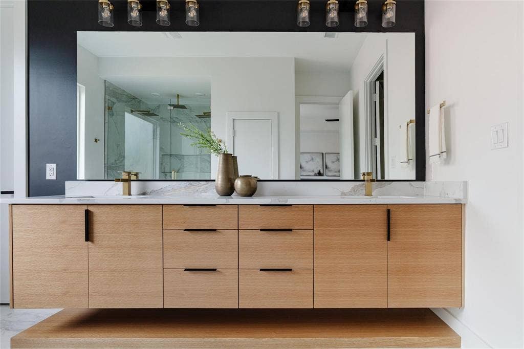 939 N Buckner Boulevard, Dallas, TX 75218 Floating wood-finish vanity with ample storage, integrated sinks, and polished gold-tone fixtures