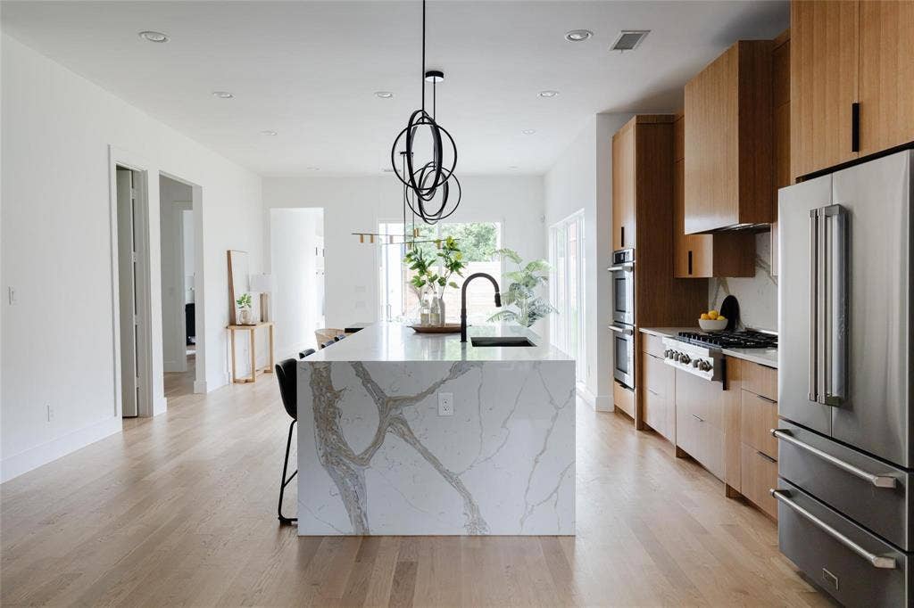 939 N Buckner Boulevard, Dallas, TX 75218 Gourmet kitchen with a waterfall island, integrated sink, stainless steel appliances, and custom wood cabinetry