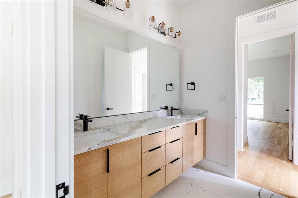 939 N Buckner Boulevard, Dallas, TX 75218 Dual vanity with wood-finish cabinetry, black hardware, and an integrated countertop with dual sinks