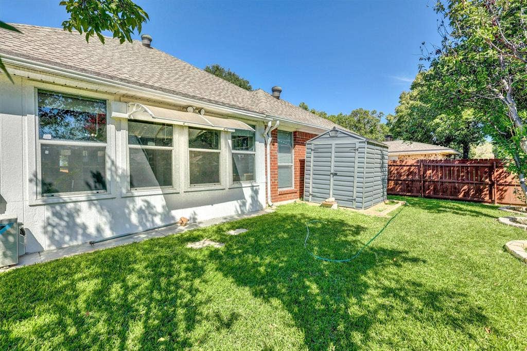 1506 Park Grove Drive, Irving, TX 75060 Expansive grassy yard with mature trees, a durable storage shed, and privacy fencing
