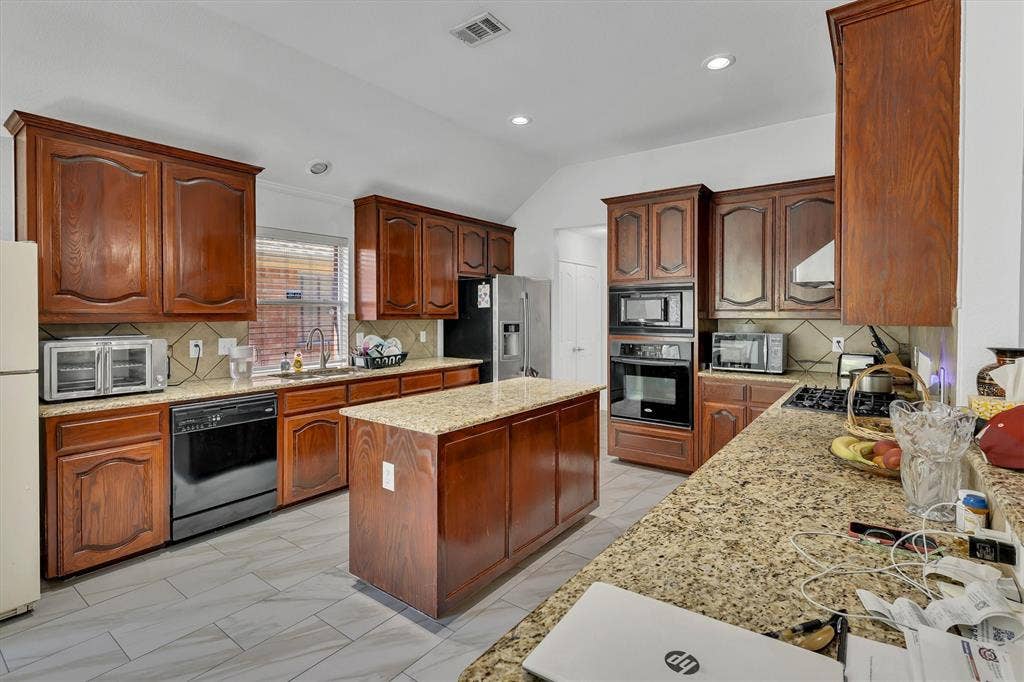 1506 Park Grove Drive, Irving, TX 75060 Spacious kitchen featuring rich wood cabinetry, granite countertops, a central island, stainless steel appliances, and tile flooring