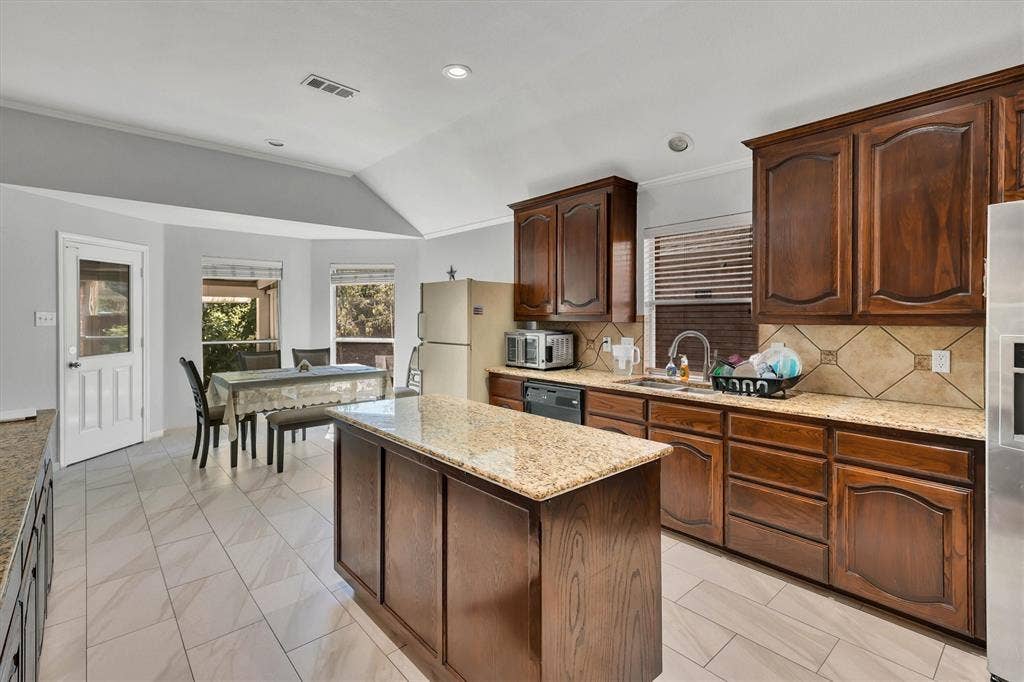 1506 Park Grove Drive, Irving, TX 75060 Central kitchen island with granite countertop, wood cabinetry, tile flooring, and integrated dining area with bay windows