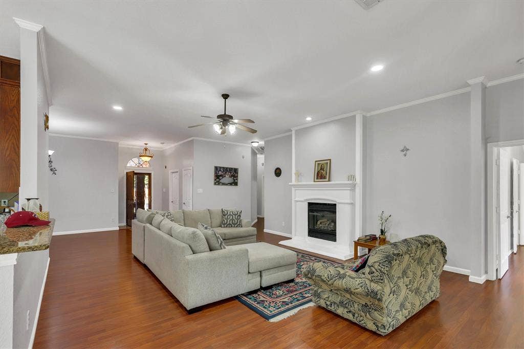 1506 Park Grove Drive, Irving, TX 75060 Spacious living area featuring wood-finish flooring, a built-in fireplace with a white mantel, recessed lighting, and crown molding