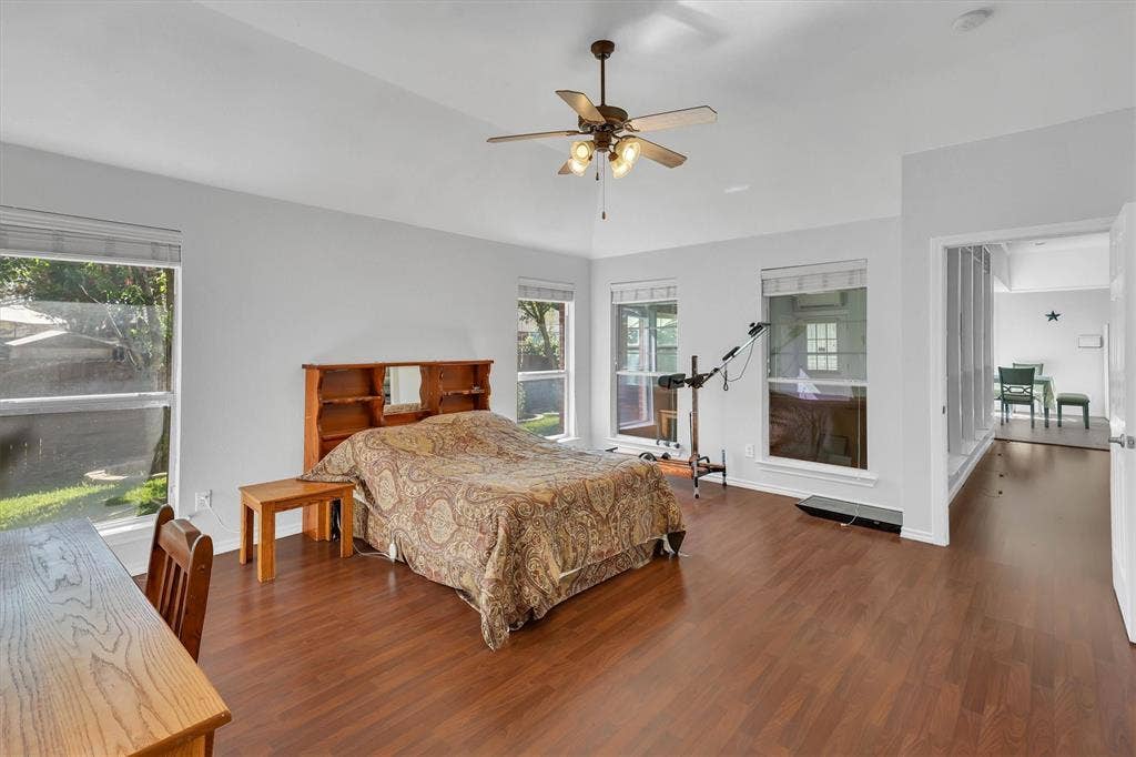 1506 Park Grove Drive, Irving, TX 75060 Vaulted ceiling featuring a ceiling fan with integrated lighting, wood-finish flooring, and multiple large windows with horizontal blinds