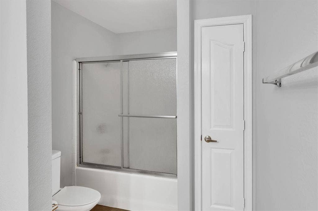 1506 Park Grove Drive, Irving, TX 75060 White bathtub with sliding glass doors, adjacent to a white toilet, and a paneled interior door