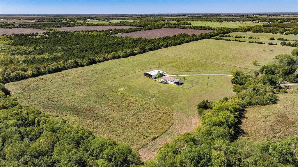 20132 County Road 818, Farmersville, TX 75442 Expansive land parcel featuring open fields, wooded borders, a residential structure, and an additional outbuilding