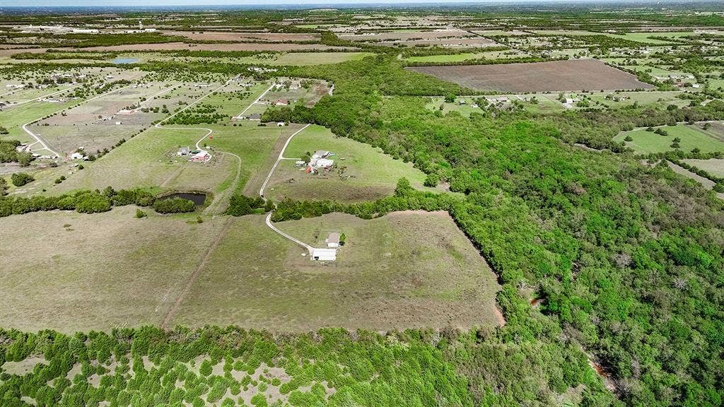 20132 County Road 818, Farmersville, TX 75442 Expansive land featuring a natural pond, lush green tree lines, and a developed parcel with a residential structure