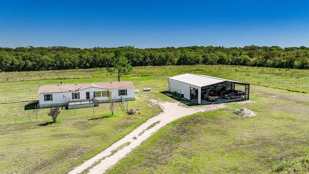 20132 County Road 818, Farmersville, TX 75442 Expansive green acreage with a single-story residence, a large detached metal structure, and a gravel drive