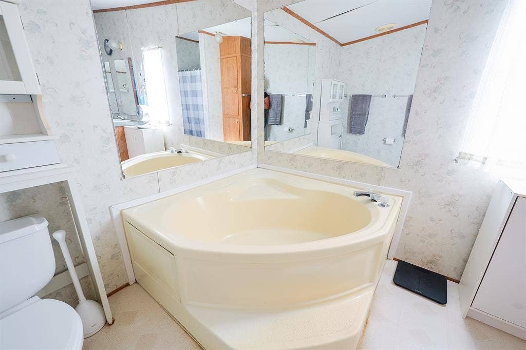 20132 County Road 818, Farmersville, TX 75442 Corner soaking tub with deck-mounted faucet and surrounding mirrors, complemented by a built-in toilet and integrated storage cabinetry