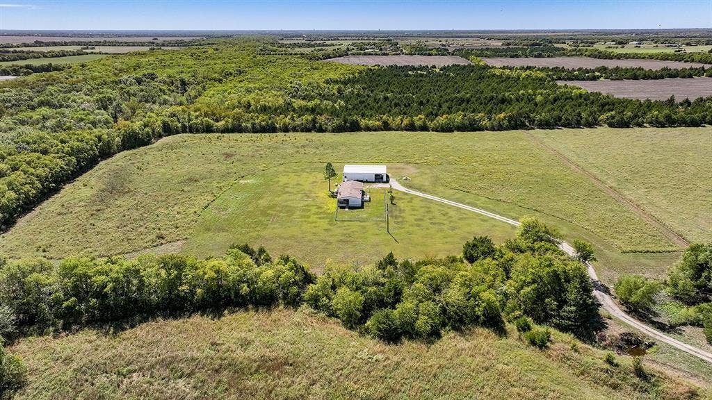 20132 County Road 818, Farmersville, TX 75442 Expansive property featuring a single-story residence with an attached garage, a detached ancillary building, a winding driveway, and surrounding natural landscapes