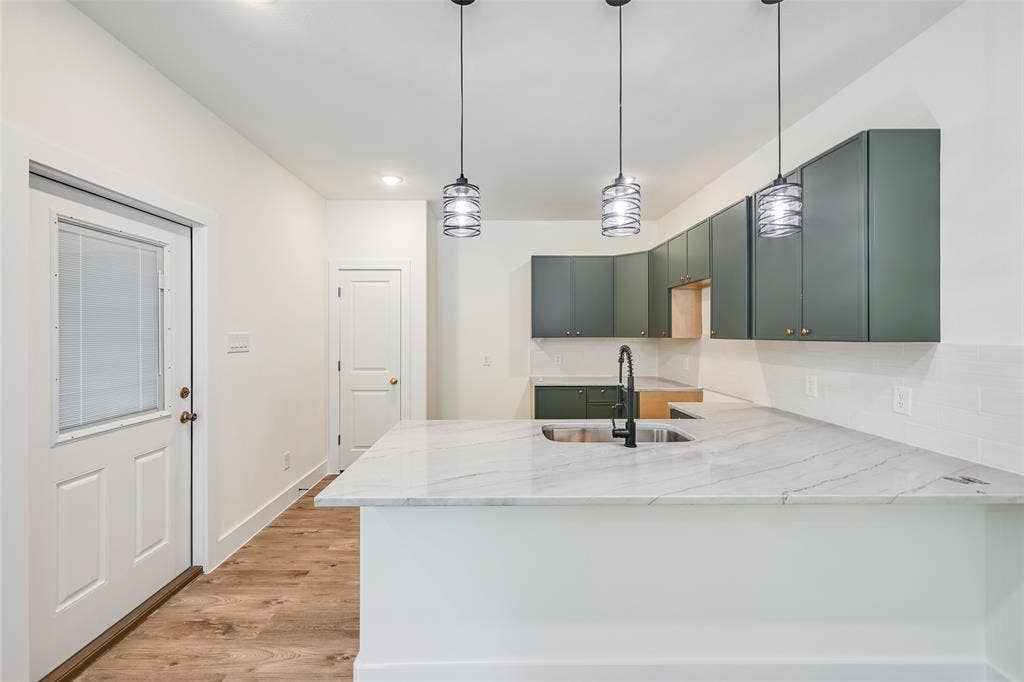 4418 Myrtle, Dallas, TX 75215 Kitchen featuring a white quartz-finish island with an undermount sink and matte black faucet, dark green cabinetry, white subway tile backsplash, and wood-finish flooring