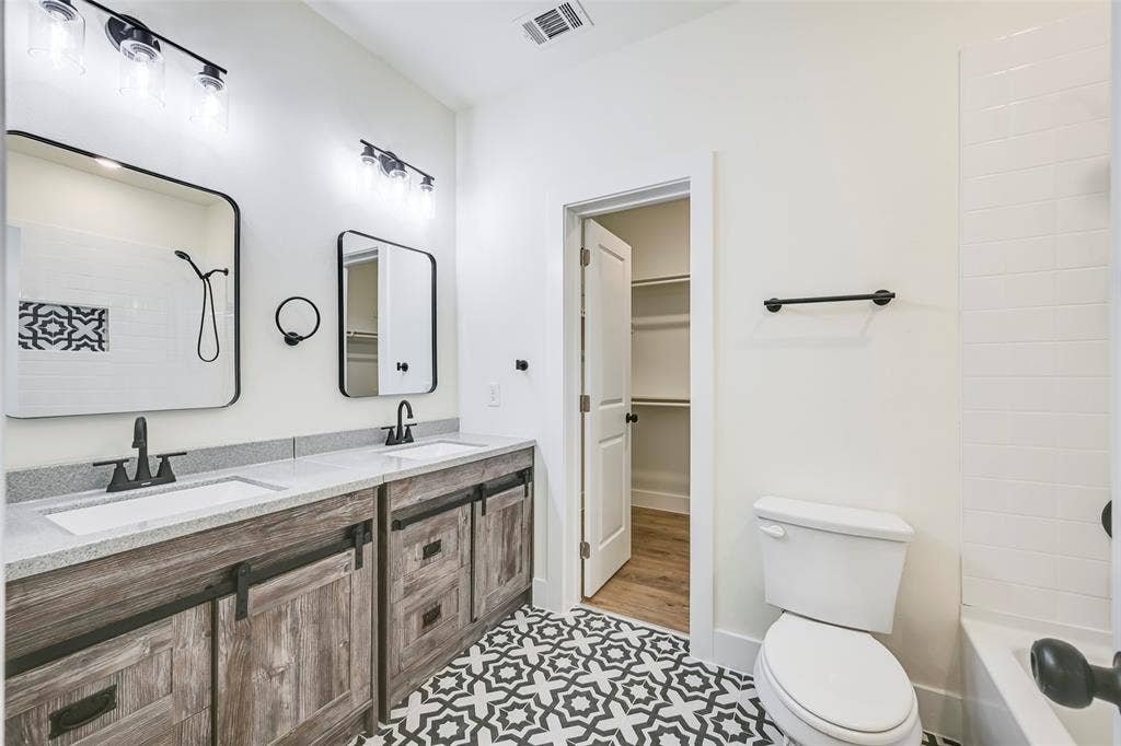 4418 Myrtle, Dallas, TX 75215 Bathroom featuring a dual vanity with light-toned countertops, wood-finish cabinetry with black hardware, and patterned floor tiling
