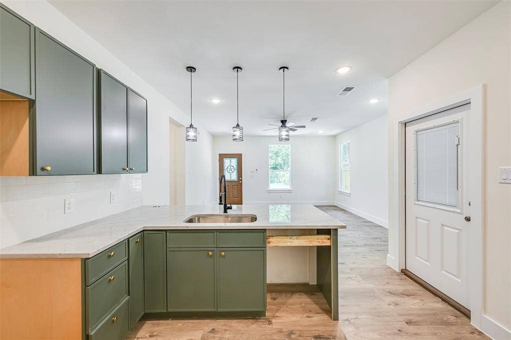 4418 Myrtle, Dallas, TX 75215 Kitchen island featuring an undermount sink, three pendant lights, and a light-toned countertop