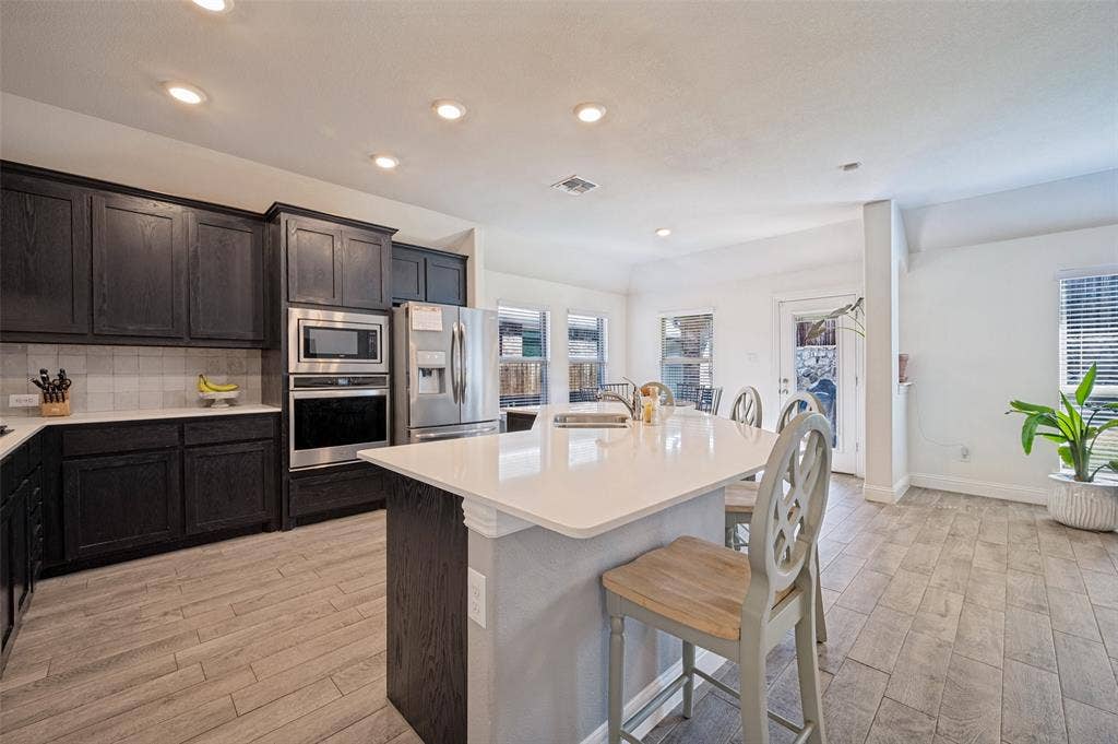 1429 Green Valley Way, Celina, TX 75009 Kitchen featuring dark wood cabinetry, stainless steel appliances, a center island with countertop seating, and light wood-finish flooring