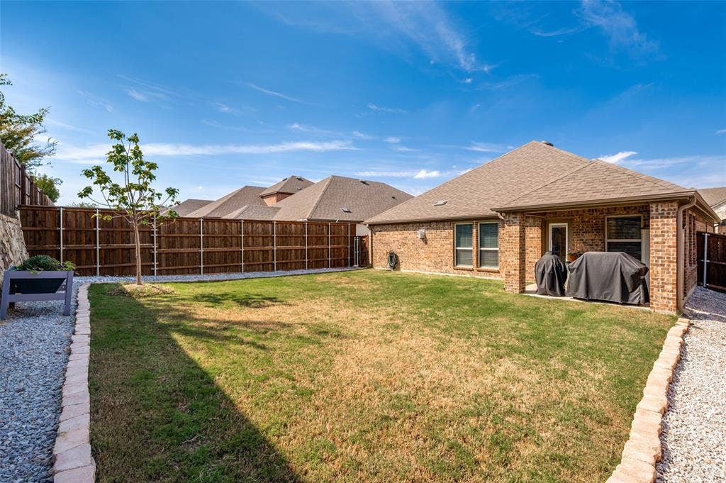 1429 Green Valley Way, Celina, TX 75009 Expansive backyard featuring a manicured lawn, gravel perimeter, brick border, and privacy fencing