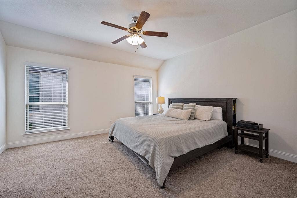 1429 Green Valley Way, Celina, TX 75009 Room featuring a vaulted ceiling with a ceiling fan, two windows with blinds, and neutral-toned carpeting