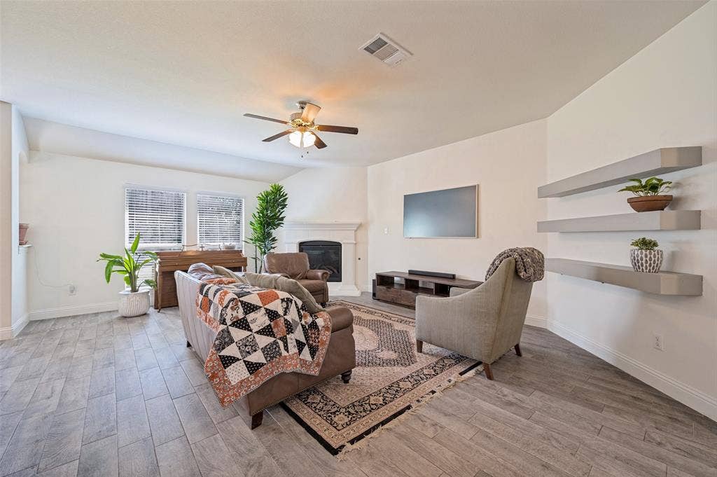 1429 Green Valley Way, Celina, TX 75009 Spacious living area featuring wood-finish flooring, a ceiling fan, and a fireplace with a white mantel