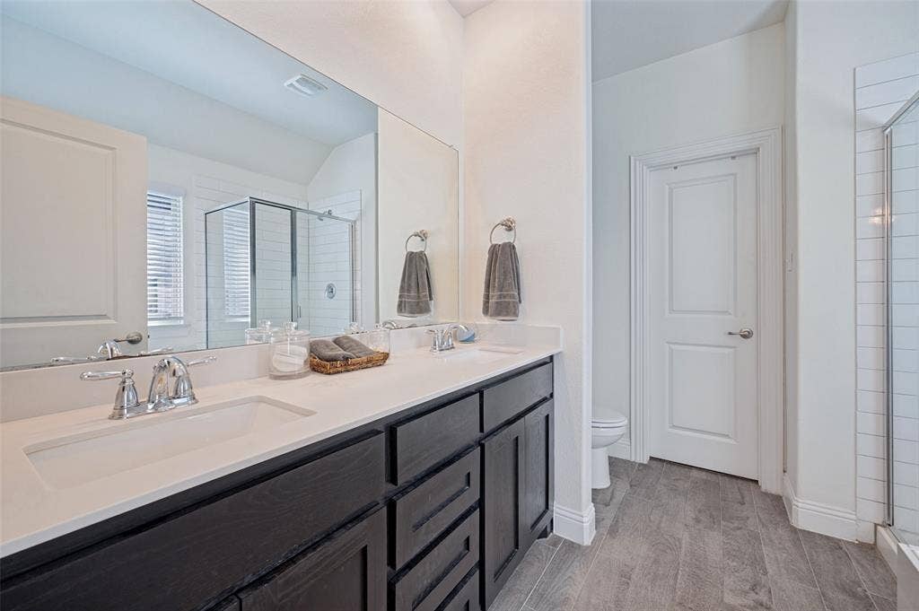 1429 Green Valley Way, Celina, TX 75009 Dual vanity with chrome fixtures and integrated sinks, extensive mirror, dark wood-finish cabinetry, white countertop, and wood-finish tile flooring