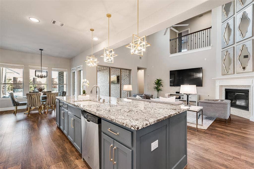 Spacious kitchen island with granite countertop, wood-finish flooring, two-story living area with fireplace, and an upper-level railing overlooking the main space