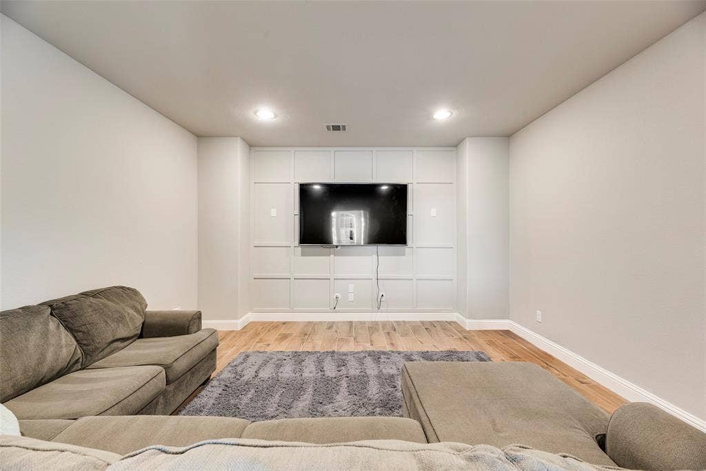 Recessed lighting illuminates the room, featuring wood-finish flooring and a built-in entertainment wall with panel detailing