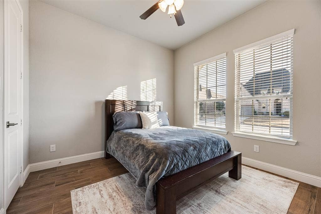 Wood-finish flooring, two large windows with blinds, ceiling fan with integrated lighting, and a paneled interior door