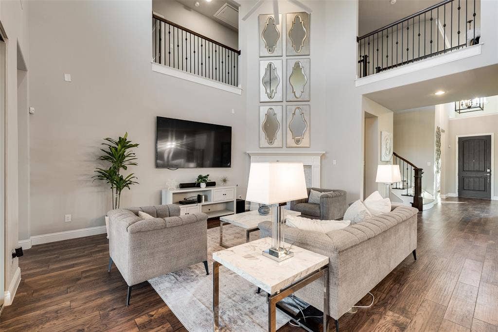 Two-story living area with wood-finish flooring, a white mantel, and an upper-level balcony with black wrought iron railing
