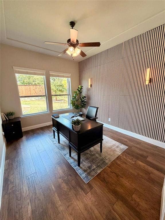 Wood-finish flooring, accent wall with vertical slat detailing, two windows, two wall-mounted sconces, and a ceiling fan with integrated lighting