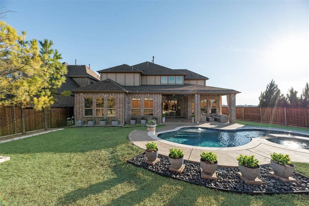 Expansive backyard featuring a manicured lawn, a freeform swimming pool, and a covered patio with brick columns