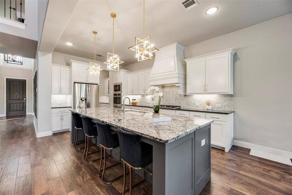 Spacious kitchen featuring an expansive center island with seating, pendant lighting, stainless steel appliances, white cabinetry, and wood-finish flooring