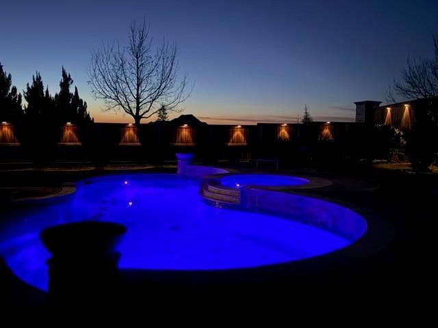 Freeform pool with integrated spa, illuminated water features, and perimeter accent lighting