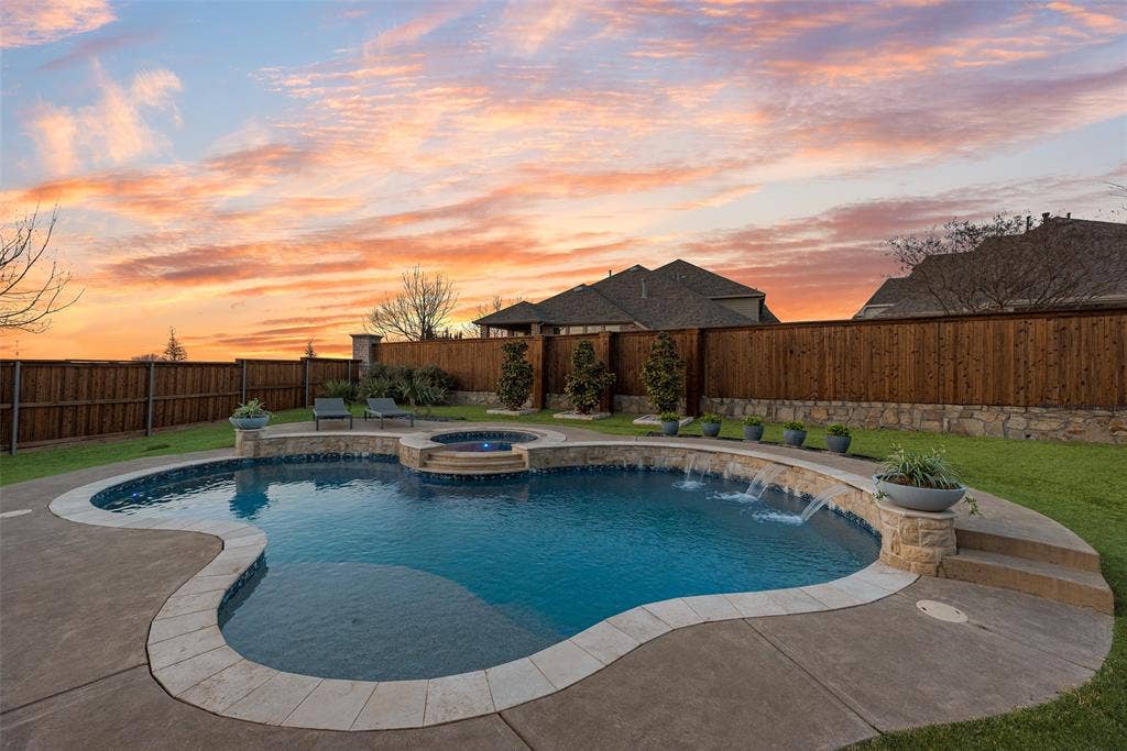 Freeform swimming pool with integrated spa, stone-capped perimeter, and multiple water features