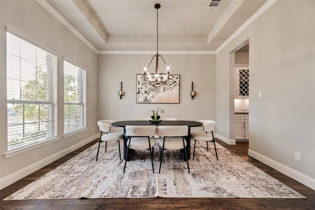 Tray ceiling, dark wood-finish flooring, two large windows with blinds, built-in cabinetry with wine rack, and a modern chandelier