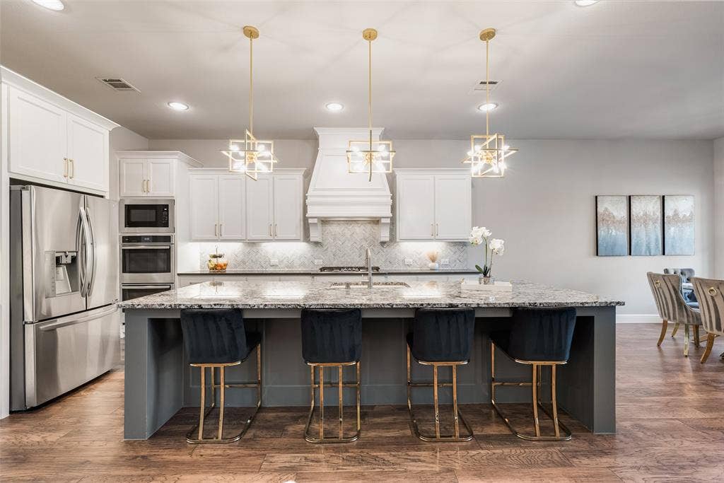 Kitchen featuring white cabinetry, stainless steel appliances, a large island with a stone countertop, and pendant lighting