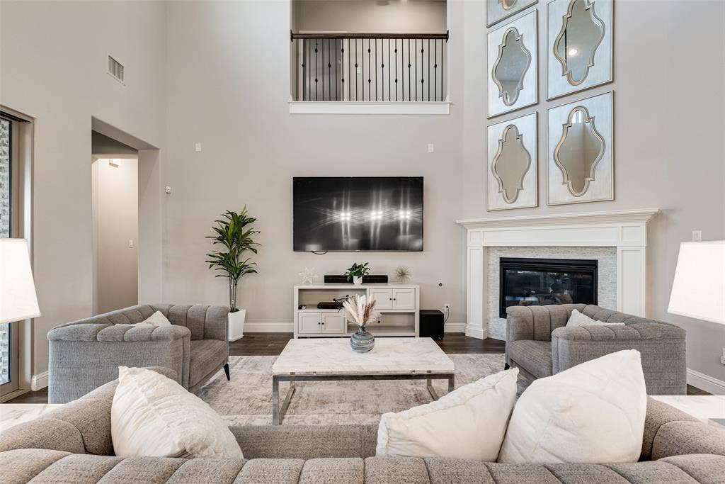 Two-story living area featuring a fireplace with a white mantel and tile surround, dark wood-finish flooring, and an upper-level balcony with a metal railing
