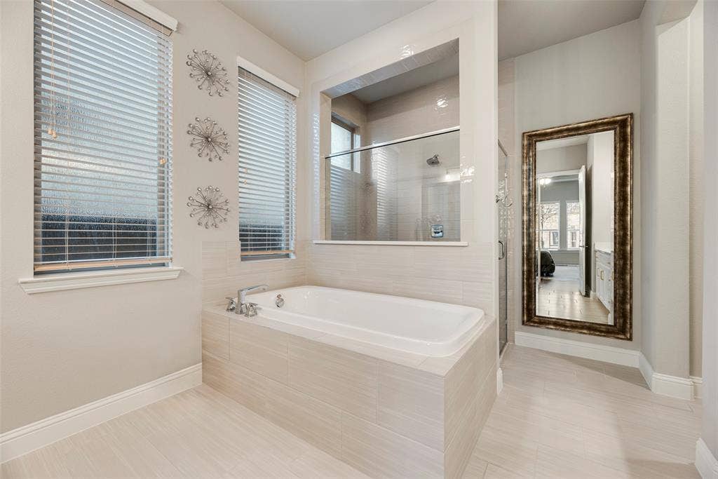 Built-in soaking tub with tile surround, walk-in shower with glass enclosure, and light-toned tile flooring