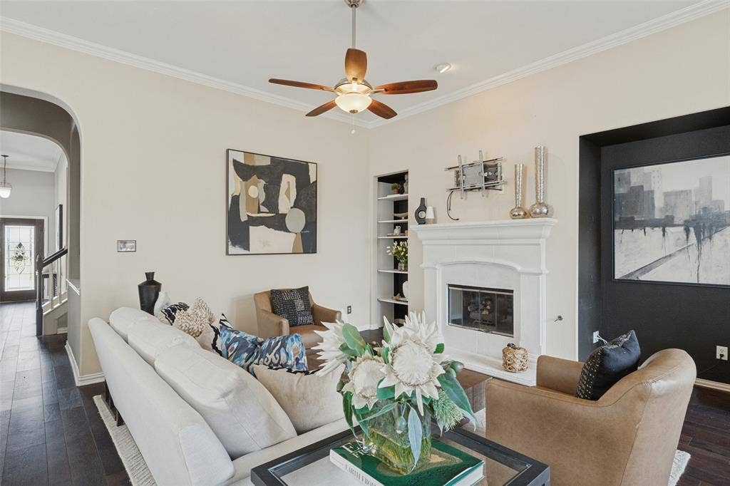 10796 Astoria Drive, Frisco, TX 75035 Inviting living room featuring a beautiful fireplace, built-in shelving, rich hardwood floors, crown molding, and high ceilings—creating a warm and comfortable gathering space.