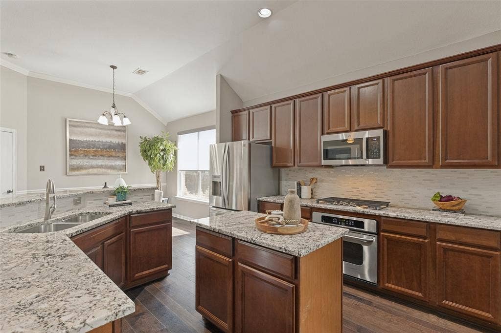 10796 Astoria Drive, Frisco, TX 75035 Well-appointed kitchen featuring granite countertops, rich wood cabinetry, stainless steel appliances, a gas cooktop, center island, and plenty of workspace, with a bright breakfast area just beyond.