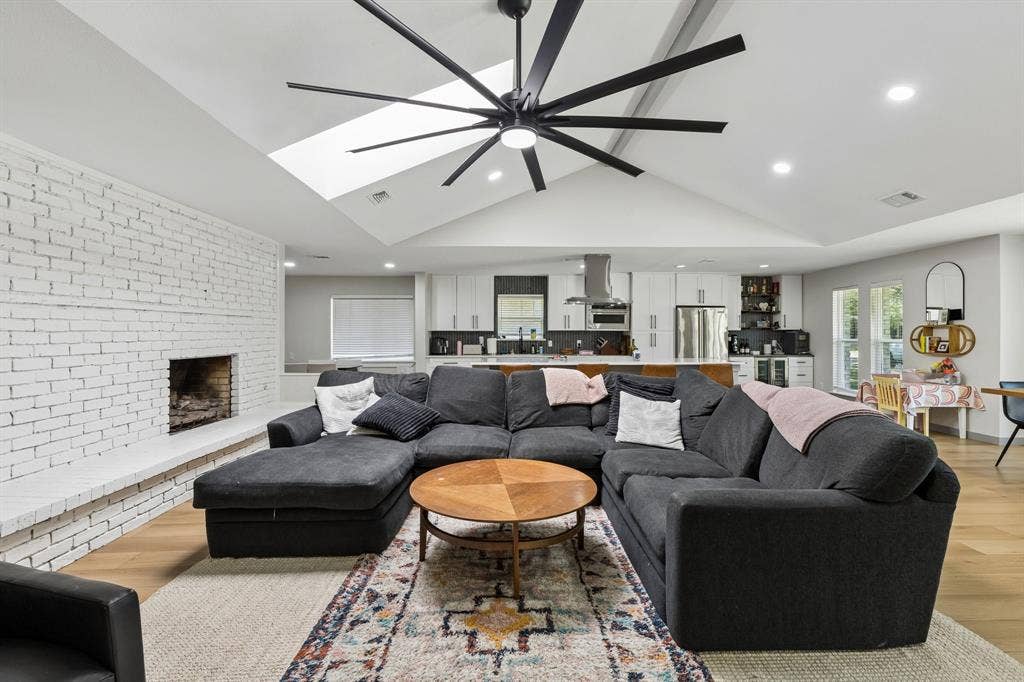 2408 Grandview Drive, Plano, TX 75075 Vaulted ceiling with skylight and large ceiling fan, white painted brick fireplace, wood-finish flooring, and recessed lighting