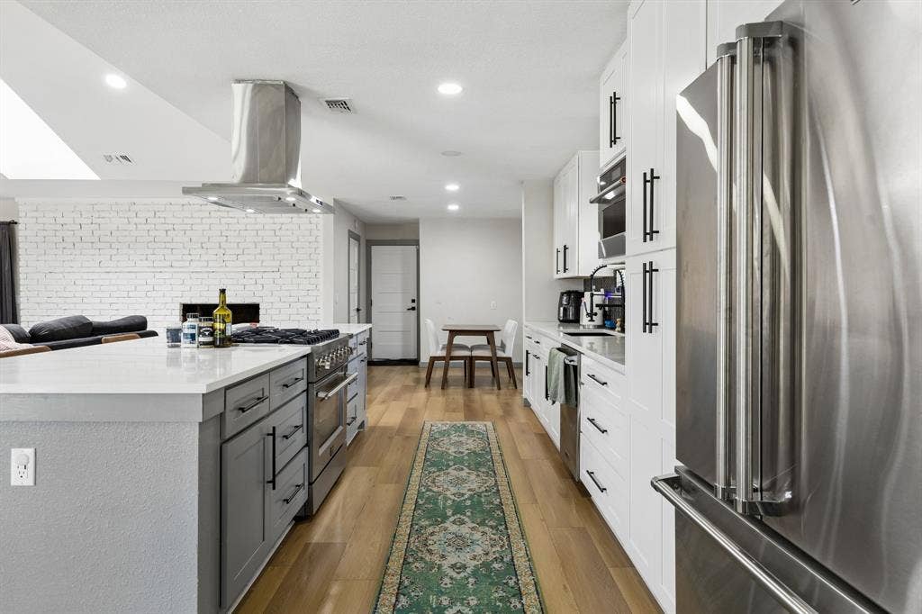 2408 Grandview Drive, Plano, TX 75075 Kitchen featuring a large center island, built-in stainless steel appliances, white cabinetry with dark hardware, and wood-finish flooring