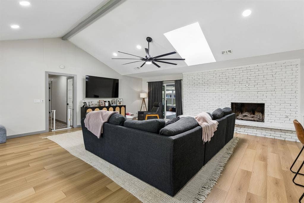 2408 Grandview Drive, Plano, TX 75075 Vaulted ceiling with exposed beam, wood-finish flooring, white-painted brick fireplace, recessed lighting, and a skylight