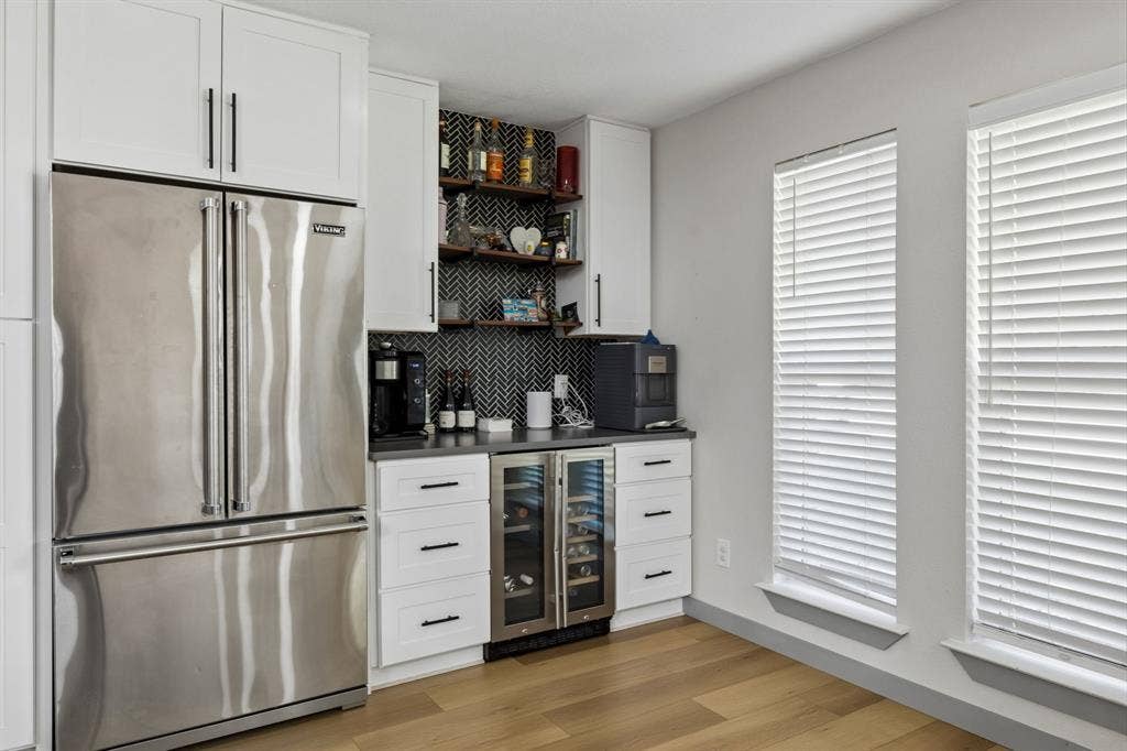2408 Grandview Drive, Plano, TX 75075 Stainless steel refrigerator, white shaker-style cabinetry, built-in beverage cooler, dark countertops, wood-finish flooring