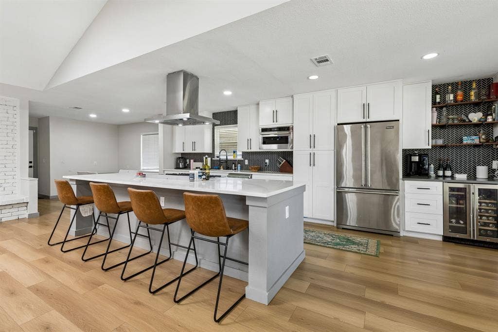 2408 Grandview Drive, Plano, TX 75075 Contemporary kitchen with wood-finish flooring, a large center island, white cabinetry, stainless steel appliances, and recessed lighting