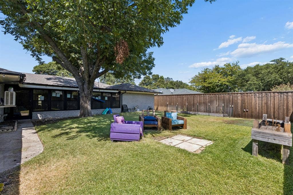 2408 Grandview Drive, Plano, TX 75075 Expansive backyard oasis featuring a mature shade tree, manicured lawn, wooden privacy fencing, and multiple entertaining spaces including built-in seating areas and a detached storage structure